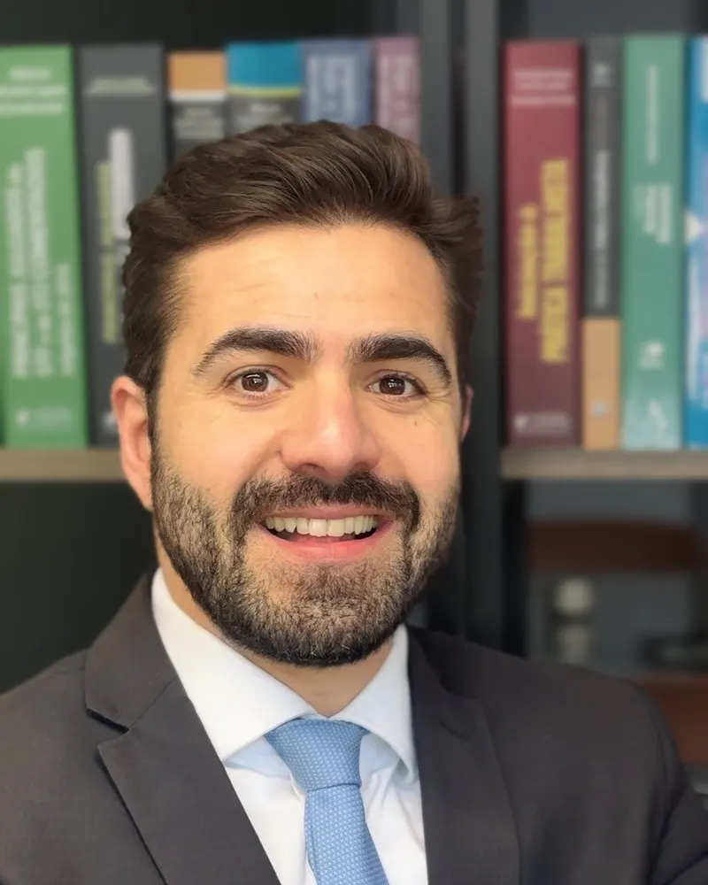 Frederico Bermúdez sorrindo em frente à estante de livros de direito do trabalho